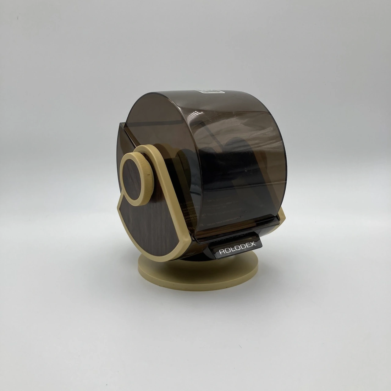 Brown translucent Rolodex desk organizer on a beige stand, viewed from the side, with a rotating card spindle