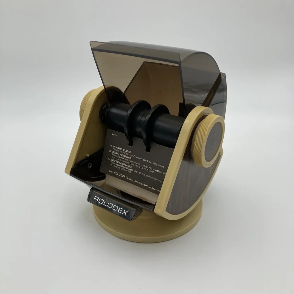 Vintage Rolodex desk index card holder with rotating spindles and beige body, used to organize contacts on a desktop.